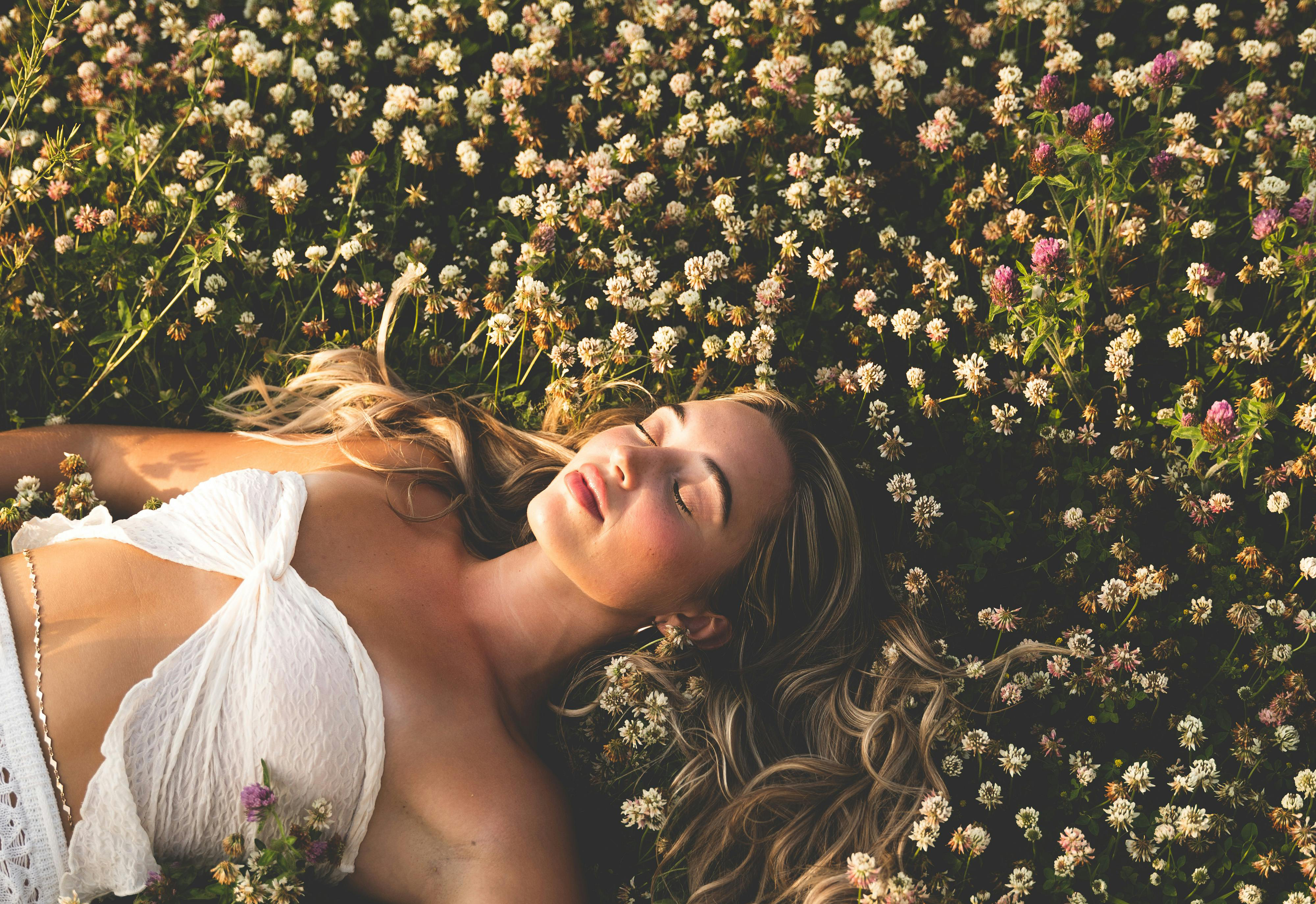 A young beautiful woman lays in a field of flowers soaking in the sunlight.